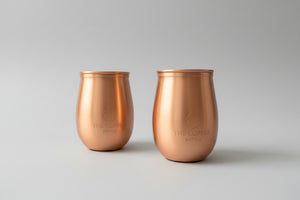 Two copper tumblers on a wooden surface with a blurred background