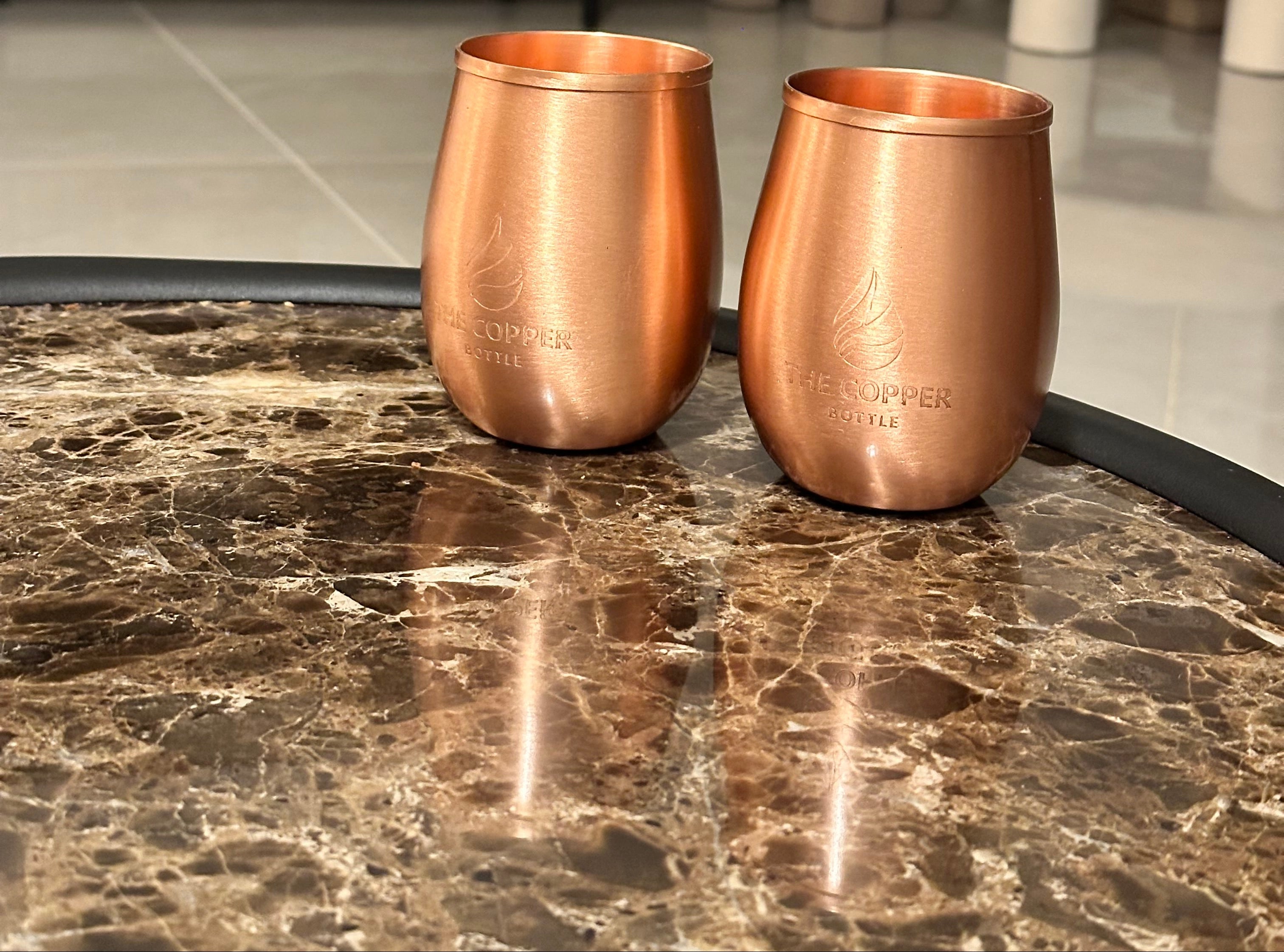 Two copper cups on a marble surface with a blurred background