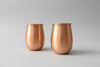 Two copper tumblers on a wooden surface with a blurred background