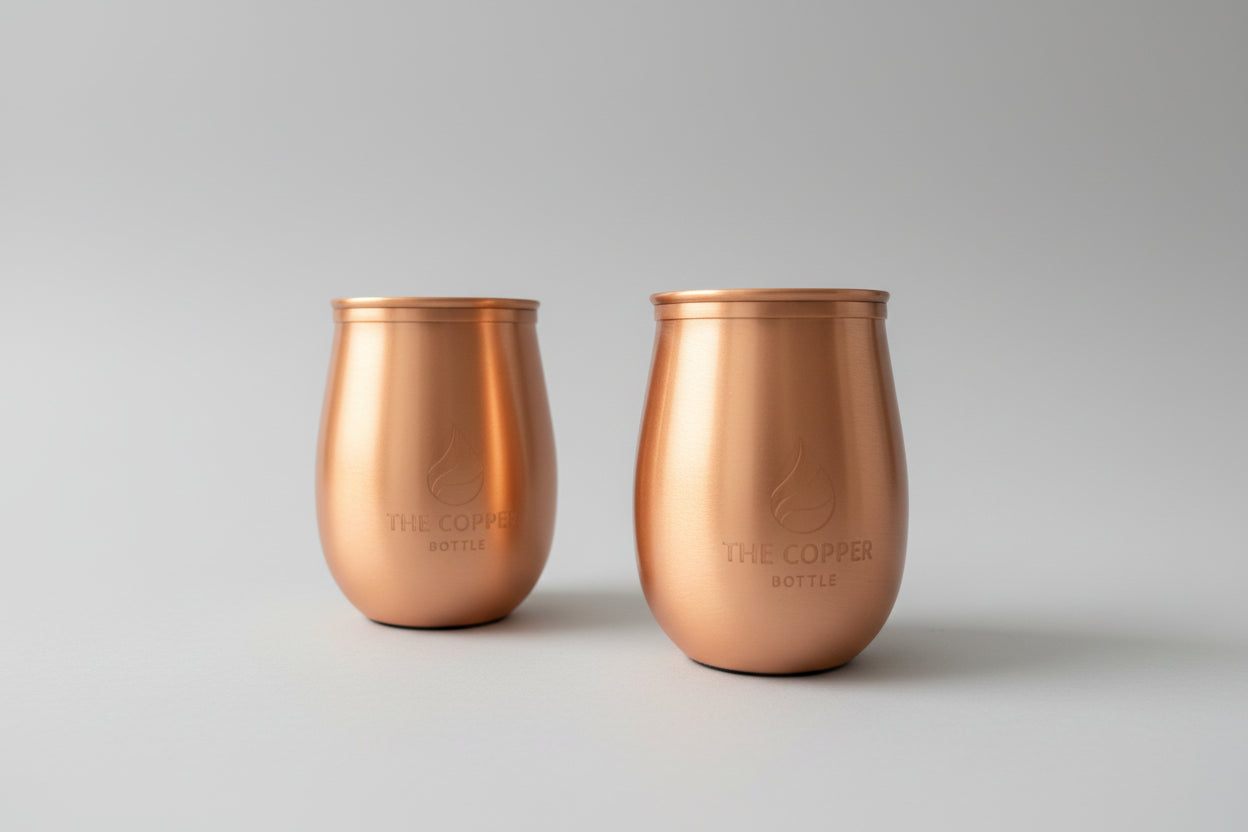 Two copper tumblers on a wooden surface with a blurred background